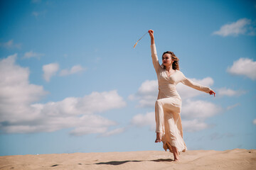 Obraz premium Young, slender girl in beige dress walks in the desert