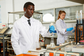 Focused man lab technician in gloves working with reagents and test tubes, woman on background