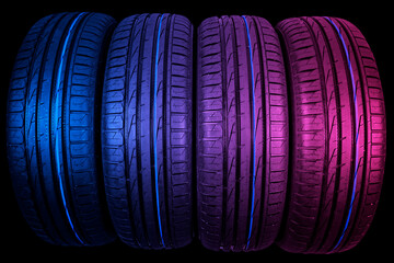 Studio shot of a set of summer car tires in pink and blue tones. Tire stack background. Car tyre protector close up. Black rubber tire. Close up black tyre profile. Car tires in a row