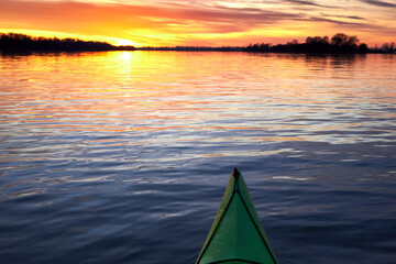 Bow of green kayak at colorful sunset over Danube river at autumn time