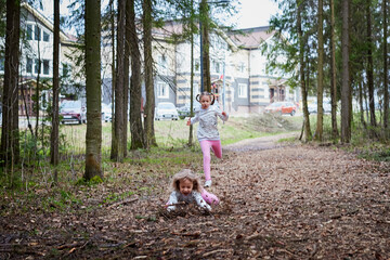 Fototapeta premium Two young girl playing and having fun together on walk in forest outdoors. Happy loving family with two sisters or female friends posing on nature landscape with with pine trees.