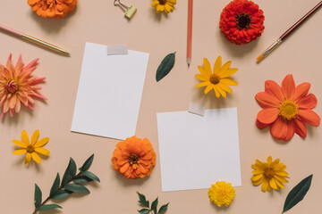 Desk with empty paper sheets, flower buds, stationery on beige background. Top view, copy space, flat lay.