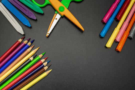 Study table. Education accessories with colorful pencils, chalk, brushes on dark school blackboard. Banner Concept Back To School.