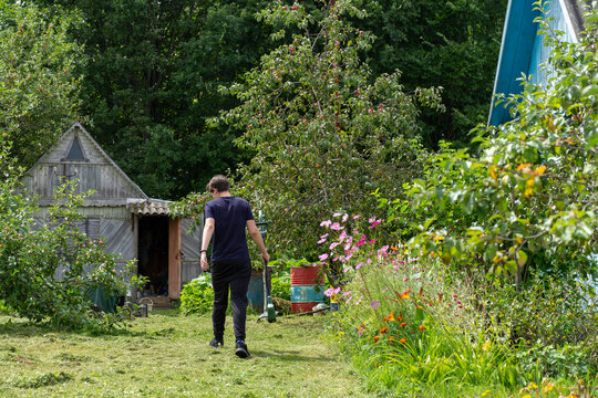 a young man walks with a trimer on the scrubbed lawn.