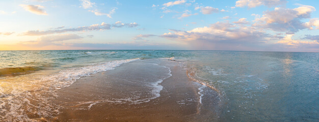 Seashore at sunset, sand is washed from two sides by waves, clouds in the sky, panorama