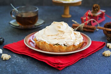 Mini tarts with custard, gooseberries and meringue in Christmas style on a red plate on a dark concrete background. Desserts meringue.
