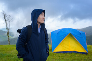 Happy traveling man enjoying and relaxing near camp tent over beautiful green mountain in rainy season, Tropical climate.