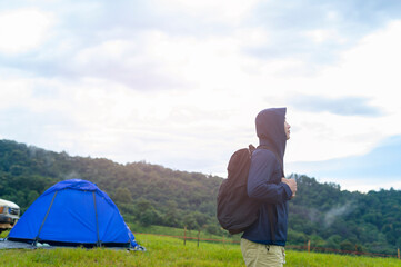 Happy traveling man enjoying and relaxing near camp tent over beautiful green mountain in rainy season, Tropical climate.