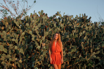 Young caucasian tourist  woman standing near cactus in red dress, smiling