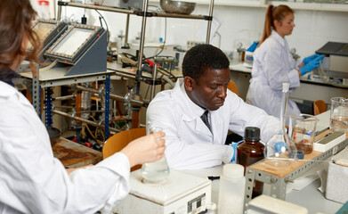 Obraz premium Focused lab technicians man writing report of chemical experiments, woman helping