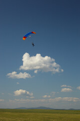 Bright parachute flying over green field on a background of blue sky and clouds.