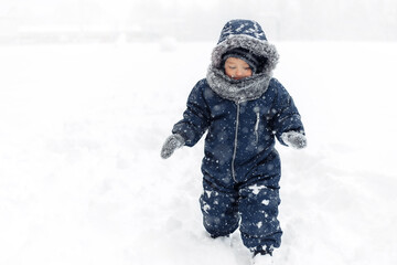 Image of cute baby boy in a warm white snow suit walking on snow.