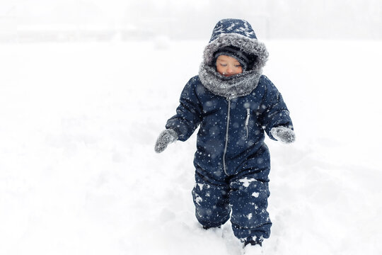 Image of cute baby boy in a warm white snow suit walking on snow.