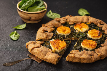 Rustic spinach and goat cheese galette on black background.
