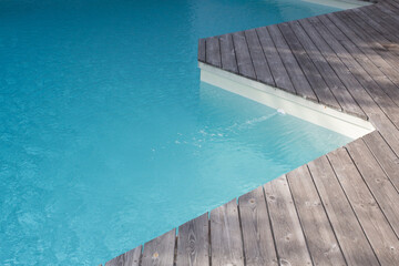 modern blue swimming pool with teak wooden flooring