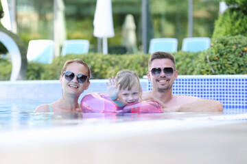 Happy family spend time at sea. Mom dad and daughter swim in pool. Girl with lifebuoy waves her hand.