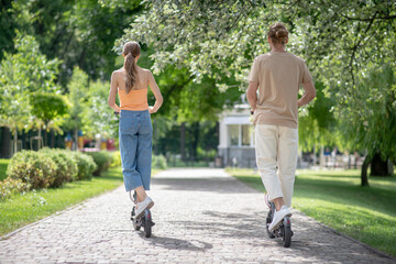 Naklejka premium Two people riding scooters in the park