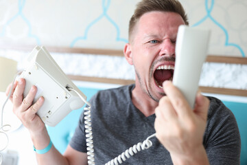 Man shouts into white phone receiver. Close-up of angry man rubbing. Guest hold phone in his hand...