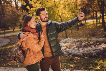 Photo of positive two people students guy embrace girl make selfie on smartphone in fall forest park wear backpack coats