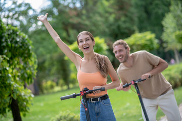 Young couple riding scooters in the park and looking excited