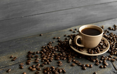Coffee cup with roasted coffee beans on wooden table background. Mug of black coffe with scattered...