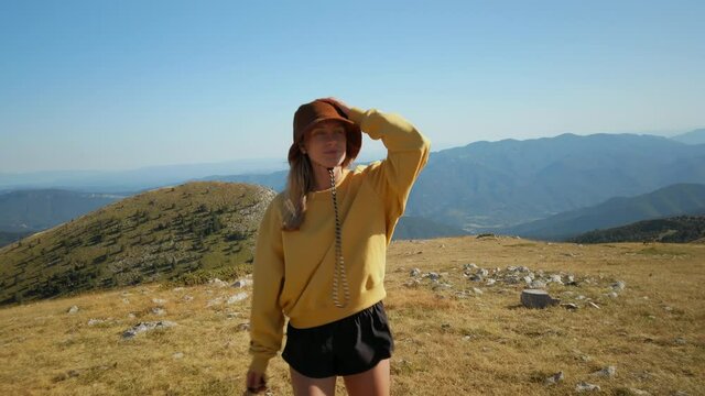 Young woman on sunny hike enjoy nature in mountains, smiling and turning face towards sun and wind. fresh breeze. Fit athletic woman in sport shorts and in yellow hoodie escape big city to nature