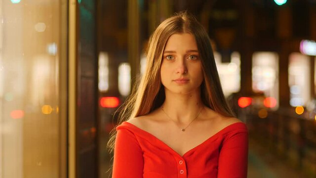 Cute pretty young girl portrait calm watch on camera wearing red dress on night city street