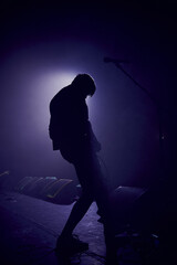A slightly blurred silhouette of a young man playing a guitar .