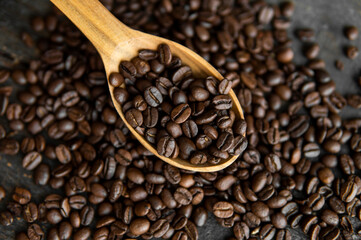 Fresh roasted arabica coffee beans in a wooden spoon and scattered coffee beans on a wooden table.