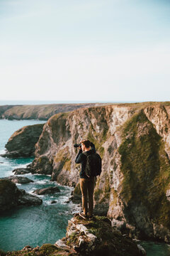 Male photographer on scenic ocean cliff, Bedruthan Steps, Cornwall, UK
