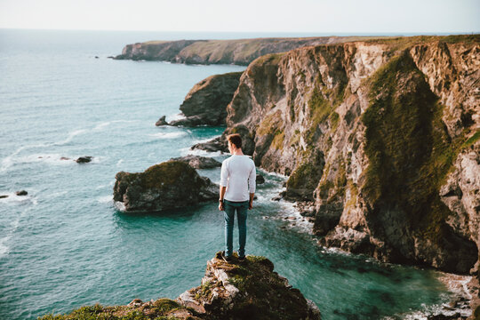 Man standing at edge of cliff over scenic ocean, Bedruthan Steps, Cornwall, UK
