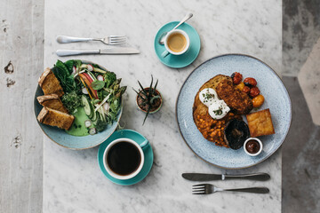 Full English breakfast and greens on toast on restaurant table
