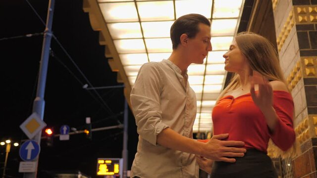 Cute young couple after night date walk saying goodbye kiss and hug and go to the sides on night city street sidewalk under building lights
