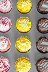 Variety of cupcakes in a metal baking tray.  Grey wood background