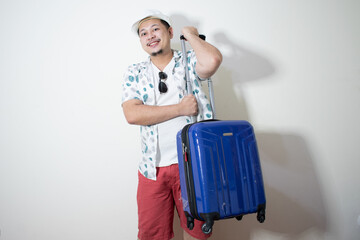 Young creative man is posing with suitcase on white background.
Holiday traveler concept