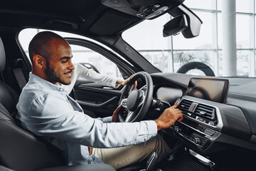 Young african american man sitting in a new car in car showroom and looking around