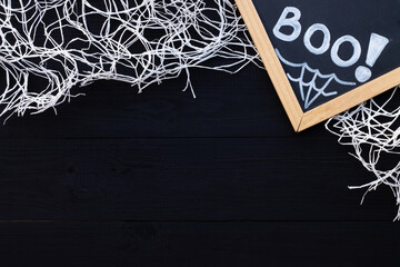 White and black Halloween flatlay. Chalk inscription BOO and spider web on a black wooden background. Copy space