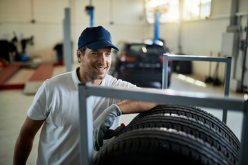 Happy car repairman working with tires in auto repair shop.