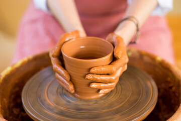 Fototapeta na wymiar hands sculpts cup from clay pot. Workshop of modeling on potter wheel.