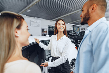 Woman car dealer explaining to buyers features of their new car