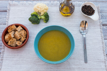 Homemade creamy vegetable soup. Made with cauliflower potatoes, peas, celery and broccoli. On the wooden table, olive oil, black pepper and croutons
