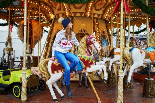 Beautiful young woman riding a horse on merry-go-round on traditional Christmas market in Paris