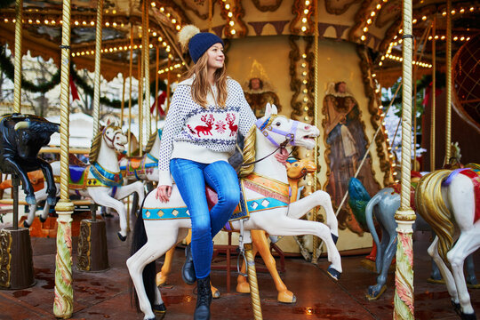 Beautiful young woman riding a horse on merry-go-round on traditional Christmas market in Paris