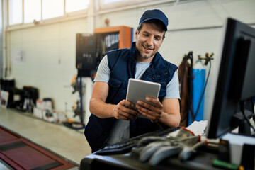 Happy auto repairman working on touchpad in a workshop.