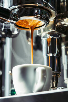 Espresso dripping from stainless steel portafilter into coffee cup
