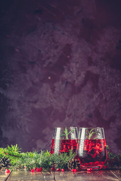 Two glasses of pomegranate drink surrounded pine branches, claret bordeaux concrete background
