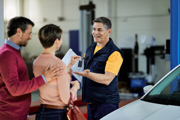 Fototapeta na wymiar Happy auto repairman receiving car key from his customers in a workshop.