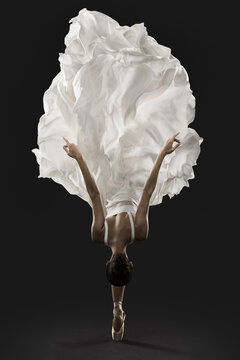 Fototapeta Ballerina Graceful Jump in White Silk Dress, Ballet Dancer Pointe Shoes in Fluttering Cloth, Black Background