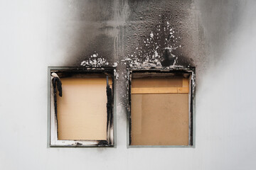 house or home fire - boarded up windows and burned facade blackened by soot of modern apartment...
