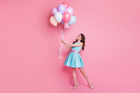 Full length photo of curly pretty lady festive event prom party hold many air balloons celebrate dreamy mood wear blue teal mini dress skirt high-heels isolated pastel pink color background